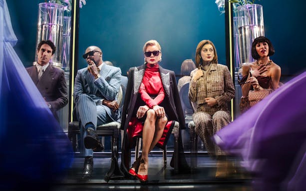 Fashion show scene from The Devil Wears Prada production with seated characters.