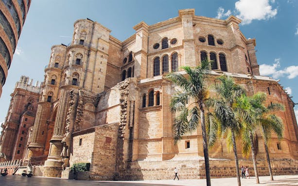 Málaga Cathedral exterior with palm trees on a sunny day.