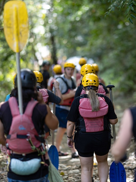 Group walking through forest with paddles for Barron River rafting tour.
