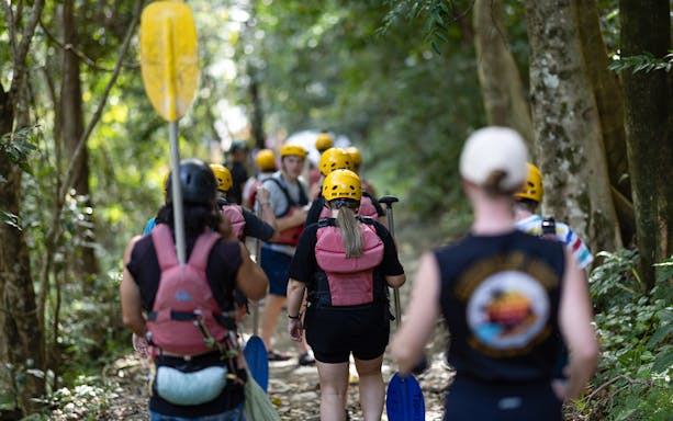 Group walking through forest with paddles for Barron River rafting tour.