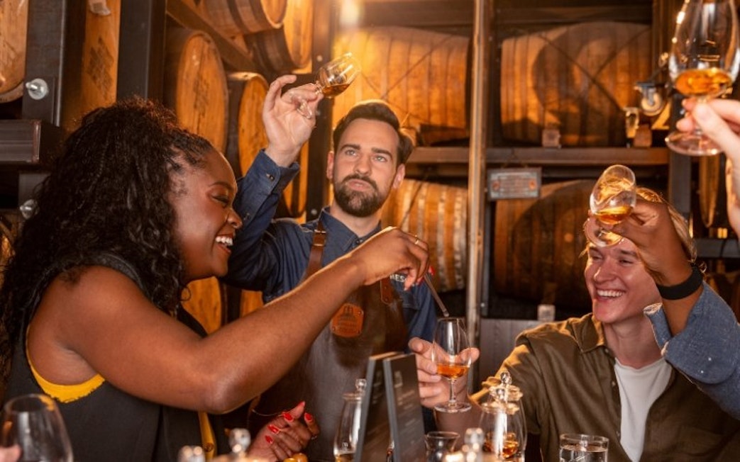 Whiskey tasting group raising glasses in a Jameson distillery cellar.