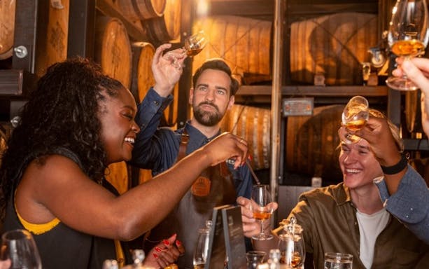Whiskey tasting group raising glasses in a Jameson distillery cellar.