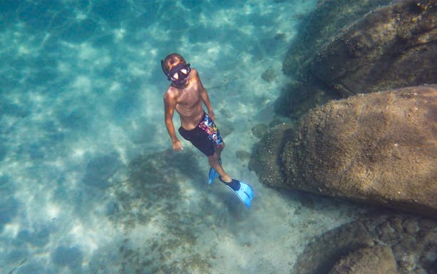 Snorkeler exploring underwater near rocks on Tavolara Island tour.