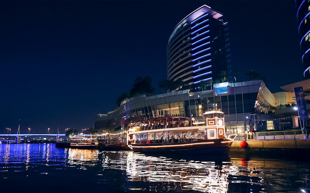Dubai Canal cruise boat illuminated at night near modern buildings.