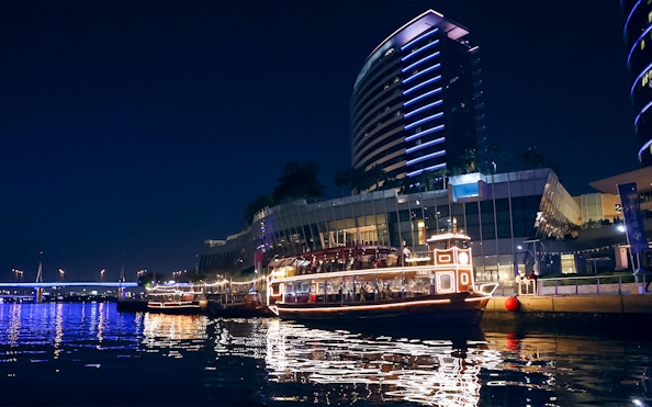 Dubai Canal cruise boat illuminated at night near modern buildings.