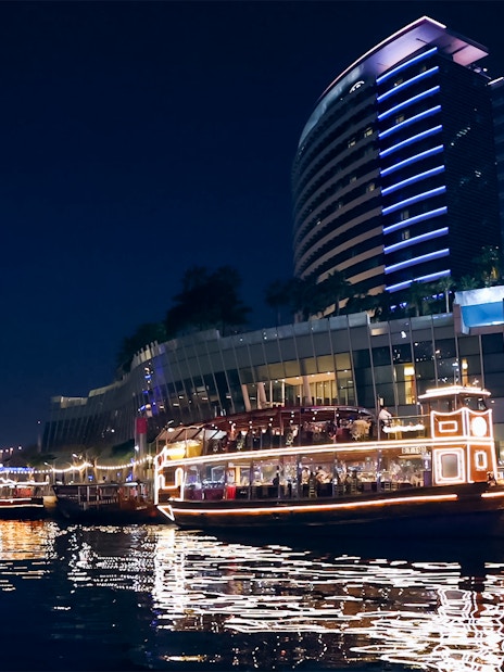 Dubai Canal cruise boat illuminated at night near modern buildings.