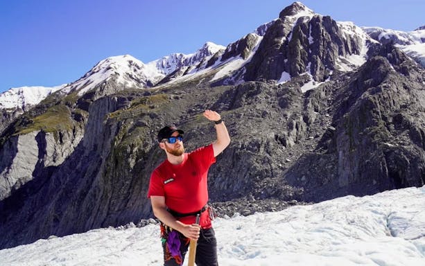 Guide leading a glacier tour with snowy mountains in the background.