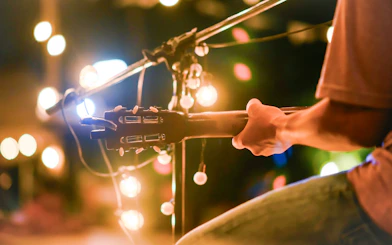 Guitarist performing under string lights at an outdoor event.