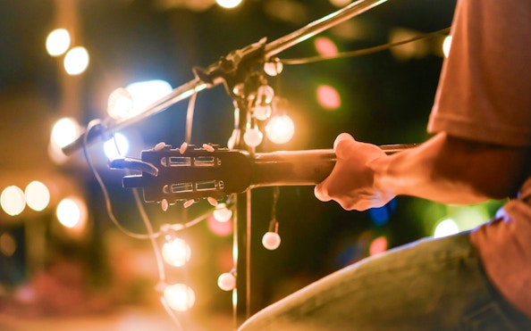 Guitarist performing under string lights at an outdoor event.