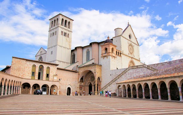 Basilica of Saint Francis of Assisi with visitors in courtyard, part of small group tour from Florence.
