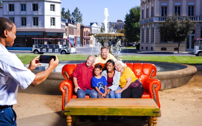 Six people on the iconic orange couch from Friends, posing for a photo in front of a fountain.