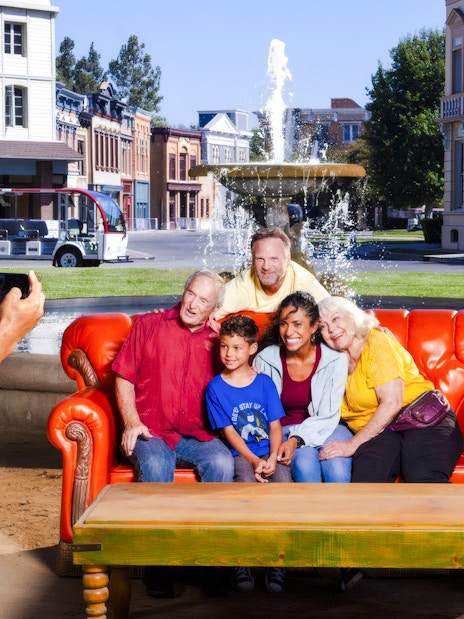 Six people on the iconic orange couch from Friends, posing for a photo in front of a fountain.