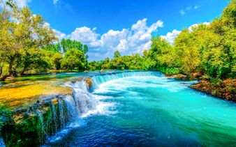 Manavgat Waterfall with lush greenery and clear blue sky.