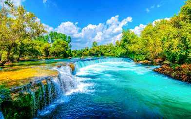 Manavgat Waterfall with lush greenery and clear blue sky.