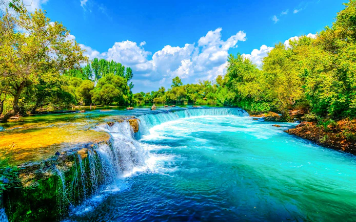 Manavgat Waterfall with lush greenery and clear blue sky.