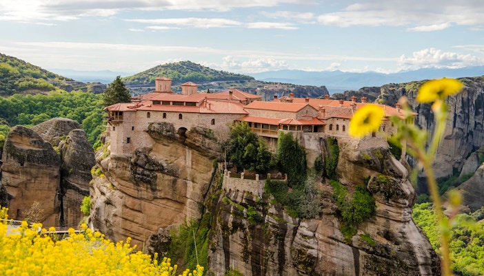 Great Meteoron Monastery perched on a rocky cliff in Meteora, Greece, surrounded by lush greenery.