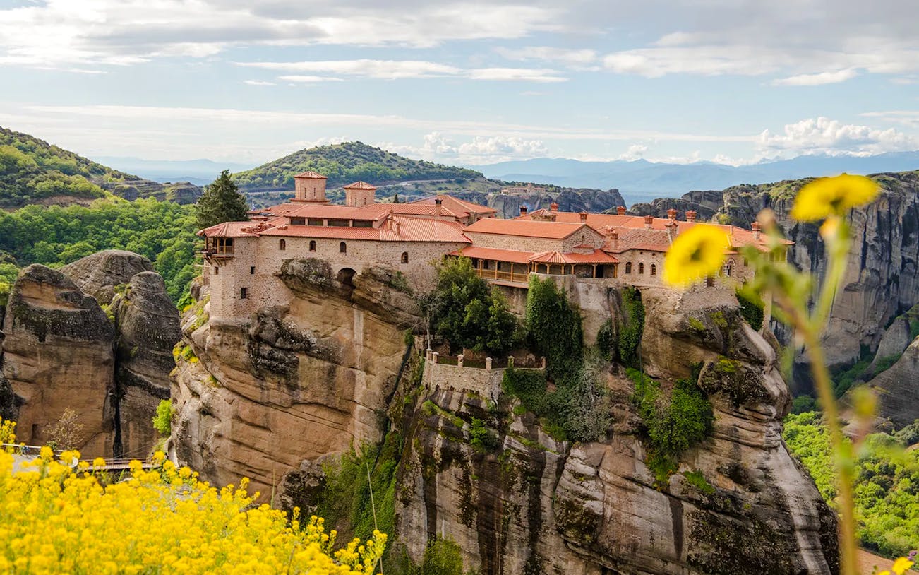 Great Meteoron Monastery perched on a rocky cliff in Meteora, Greece, surrounded by lush greenery.