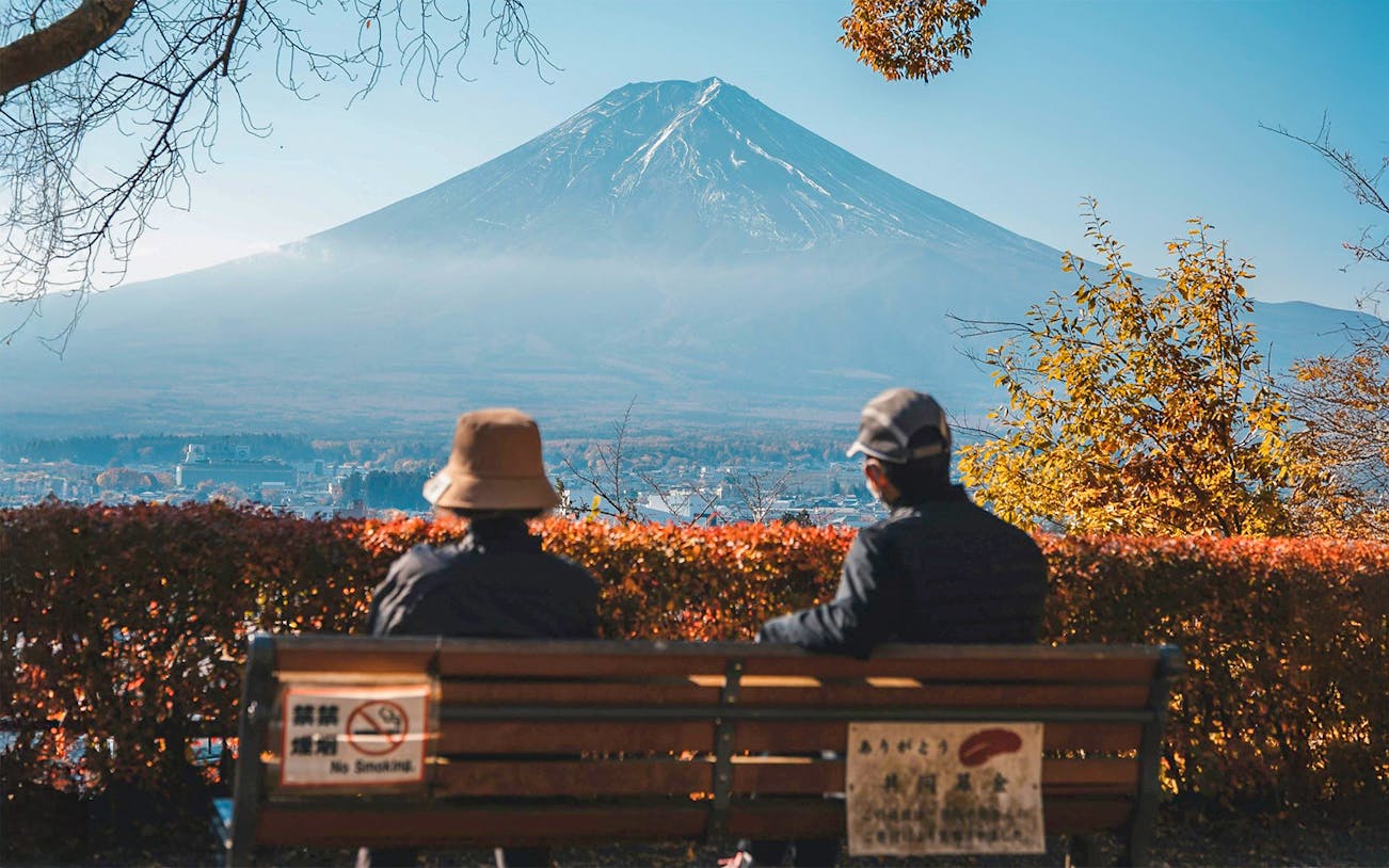 Two people sitting on a bench with a view of Mt. Fuji in Hakone, Japan.