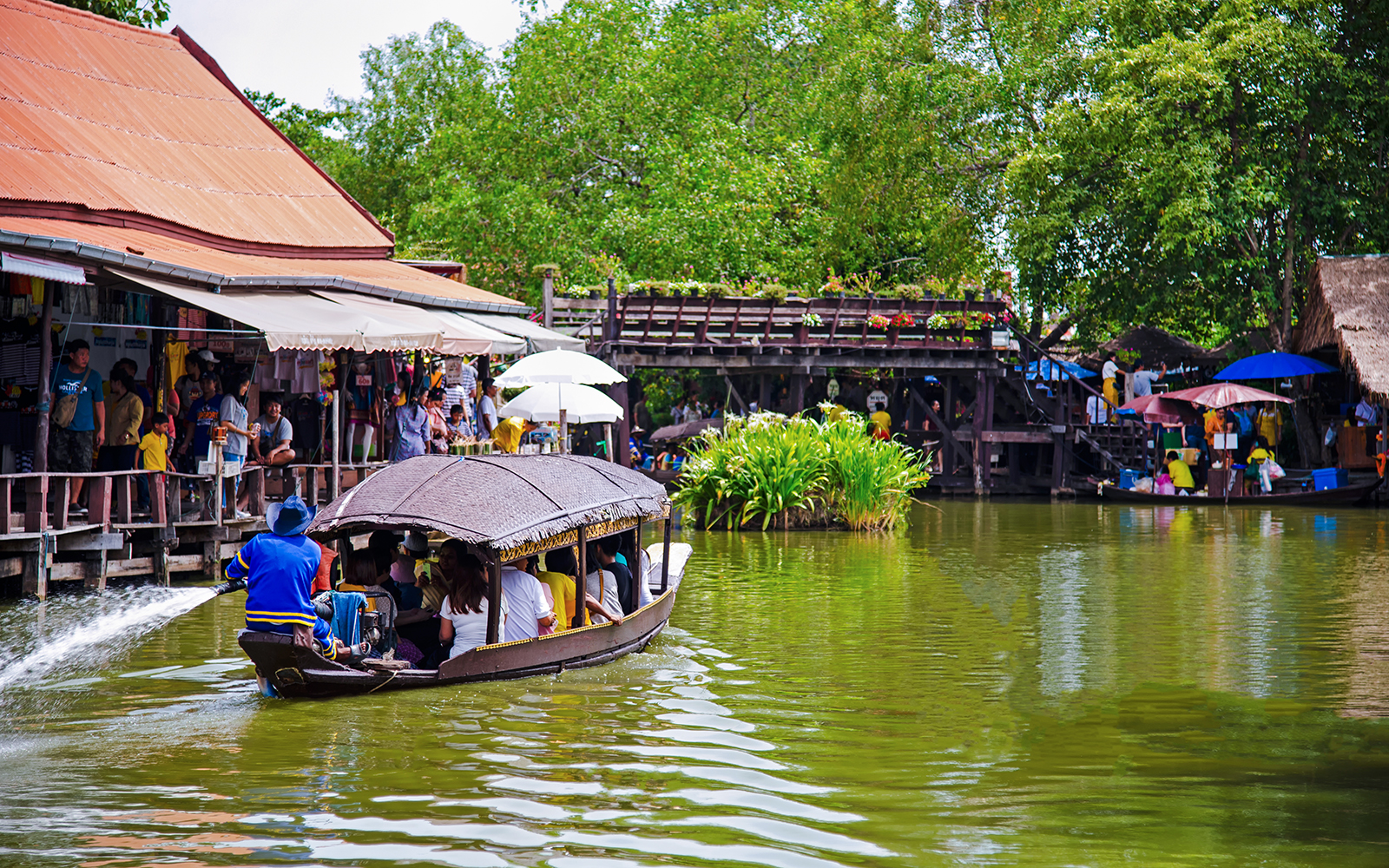 Boat navigating Ayutthaya Floating Market with shops and visitors along the water.