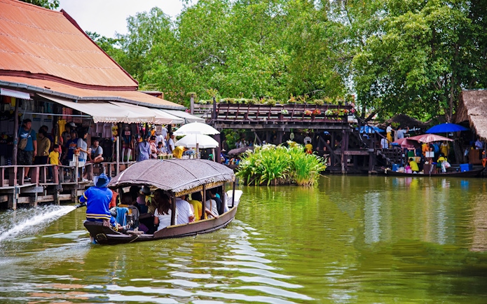 Boat navigating Ayutthaya Floating Market with shops and visitors along the water.
