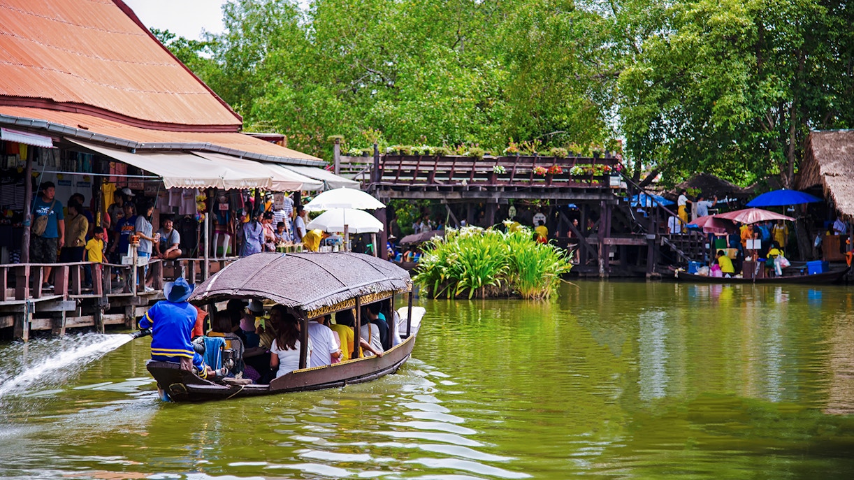 Boat navigating Ayutthaya Floating Market with shops and visitors along the water.