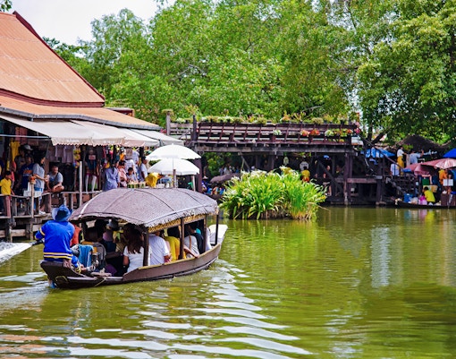 Boat navigating Ayutthaya Floating Market with shops and visitors along the water.