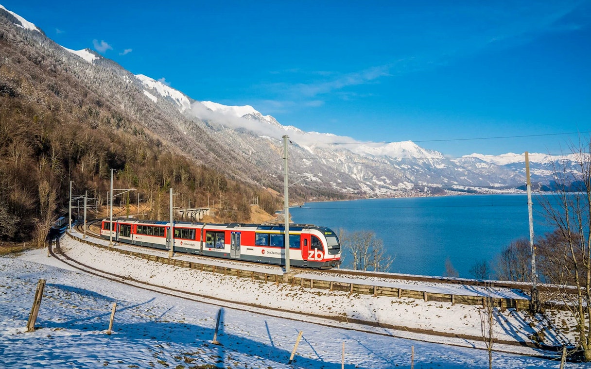 Train on Lucerne–Interlaken Express route with snowy mountains and lake views.