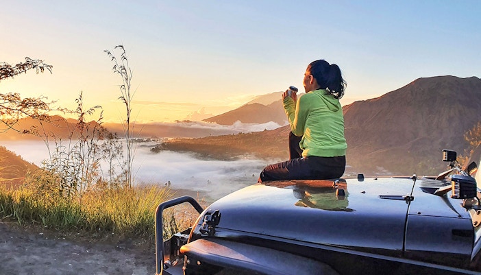 Woman sit on car hood while enjoy mount batur