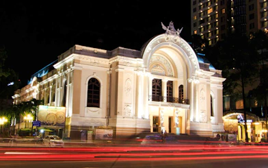 Ho Chi Minh Municipal Theater illuminated at night with light trails from passing traffic.