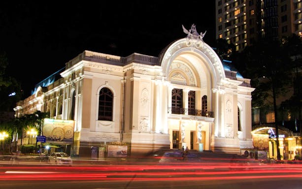 Ho Chi Minh Municipal Theater illuminated at night with light trails from passing traffic.