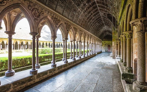 Cloister arches of Mont Saint-Michel Abbey, France, with garden view.