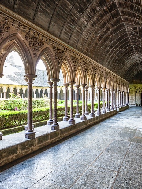Cloister arches of Mont Saint-Michel Abbey, France, with garden view.