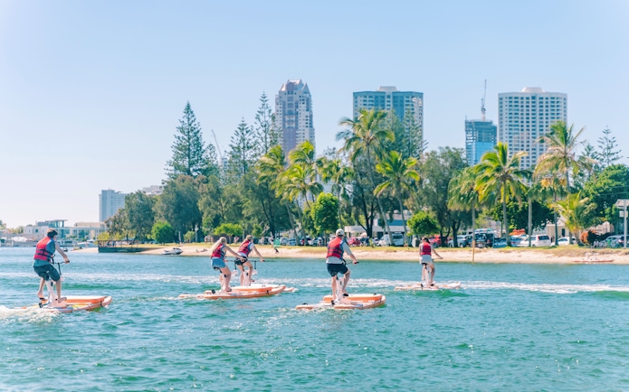 Tourists riding waterbikes on the Gold Coast with city skyline in the background.