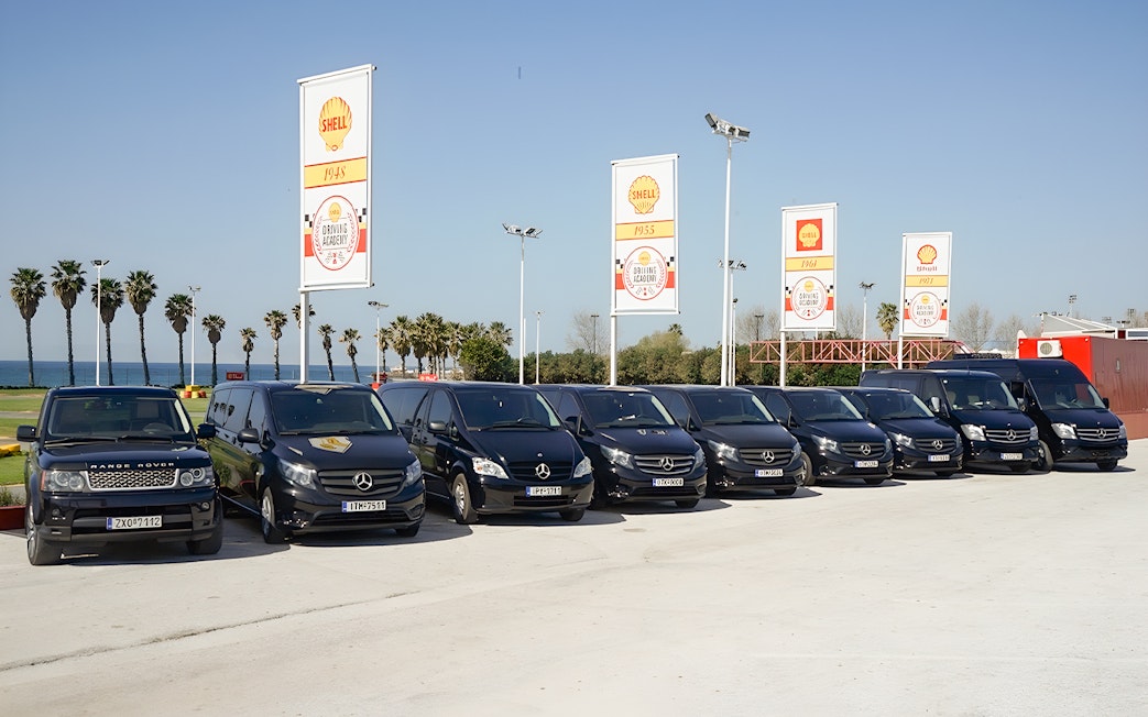 Fleet of tour vehicles for Sensational Meteora Private Day Tour from Athens, parked near palm trees.