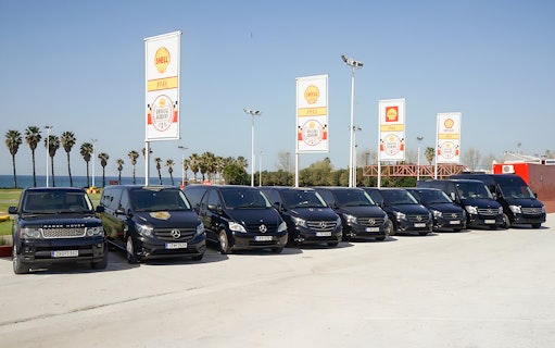 Fleet of tour vehicles for Sensational Meteora Private Day Tour from Athens, parked near palm trees.