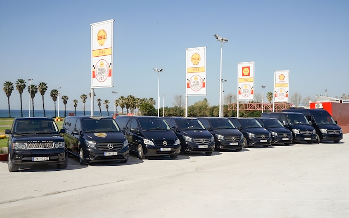 Fleet of tour vehicles for Sensational Meteora Private Day Tour from Athens, parked near palm trees.