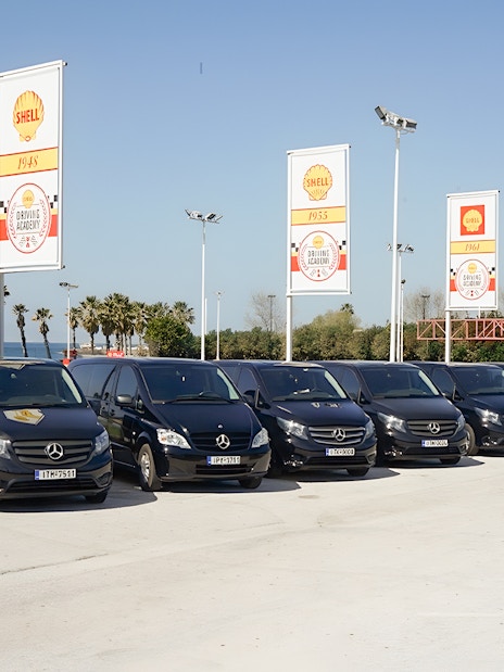 Fleet of tour vehicles for Sensational Meteora Private Day Tour from Athens, parked near palm trees.