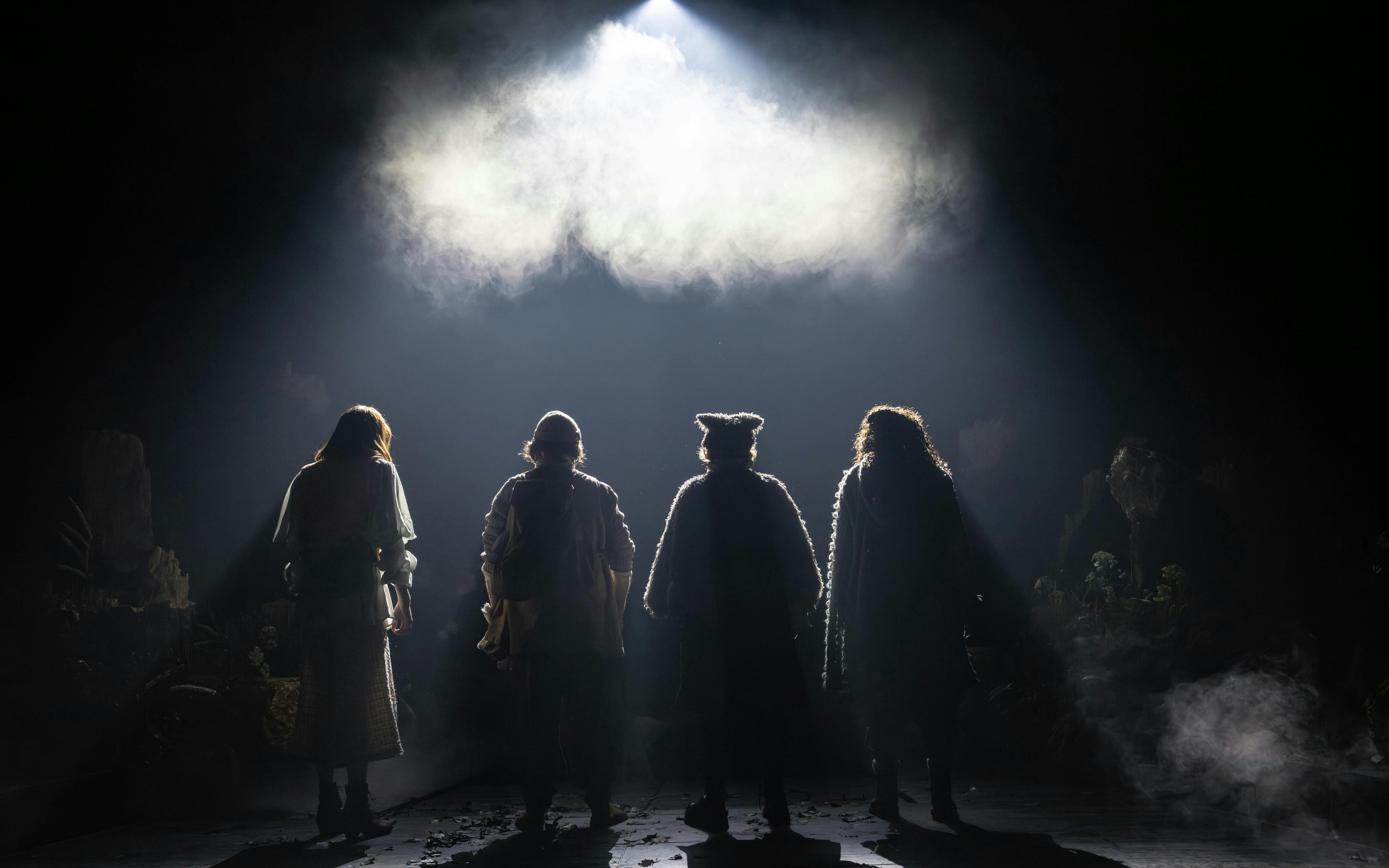 Four actors in costume stand on a dimly lit stage for Into The Woods production.