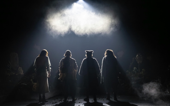 Four actors in costume stand on a dimly lit stage for Into The Woods production.