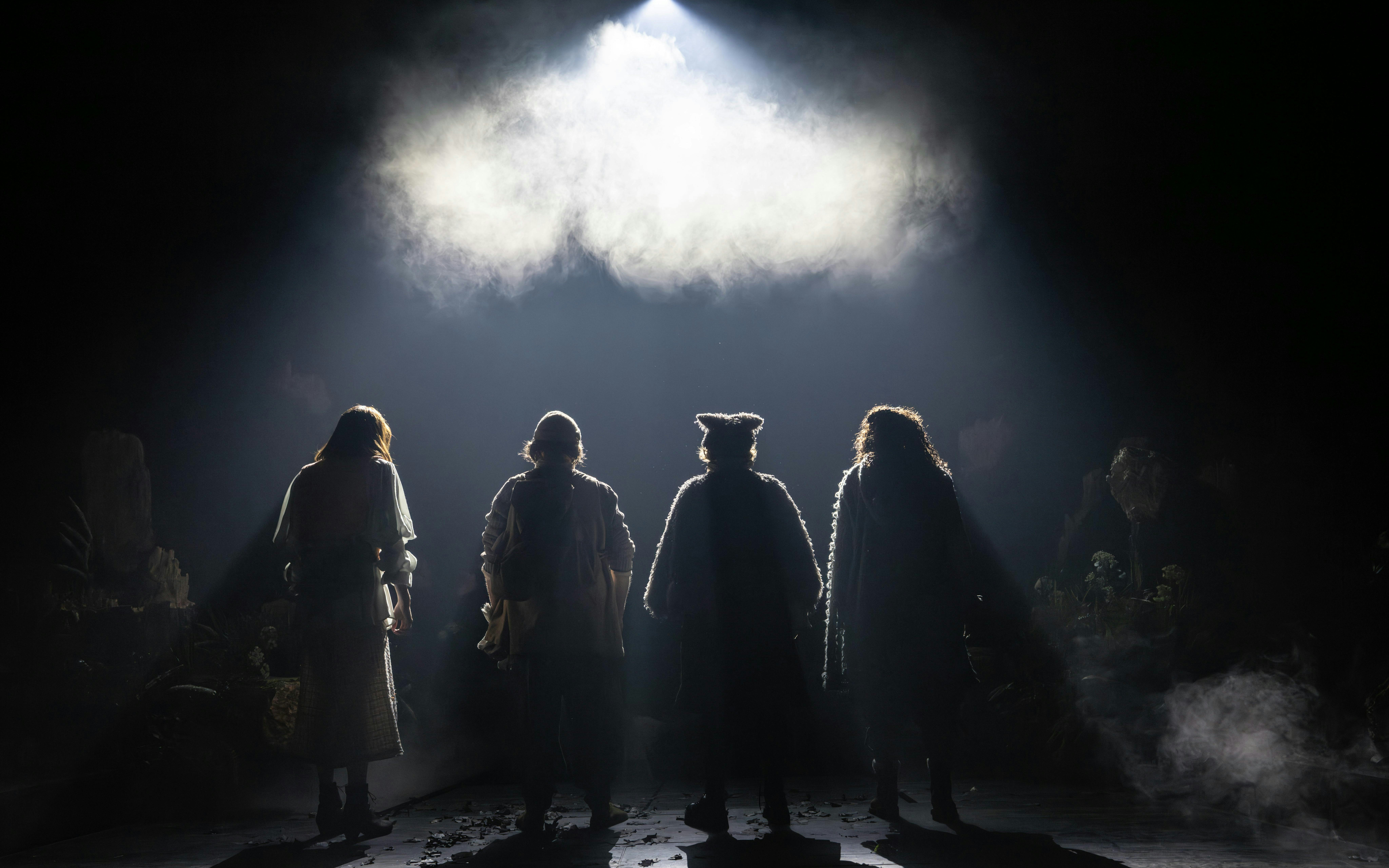 Four actors in costume stand on a dimly lit stage for Into The Woods production.
