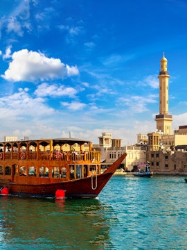 Traditional dhow boat on Dubai Creek with cityscape and mosque in background.
