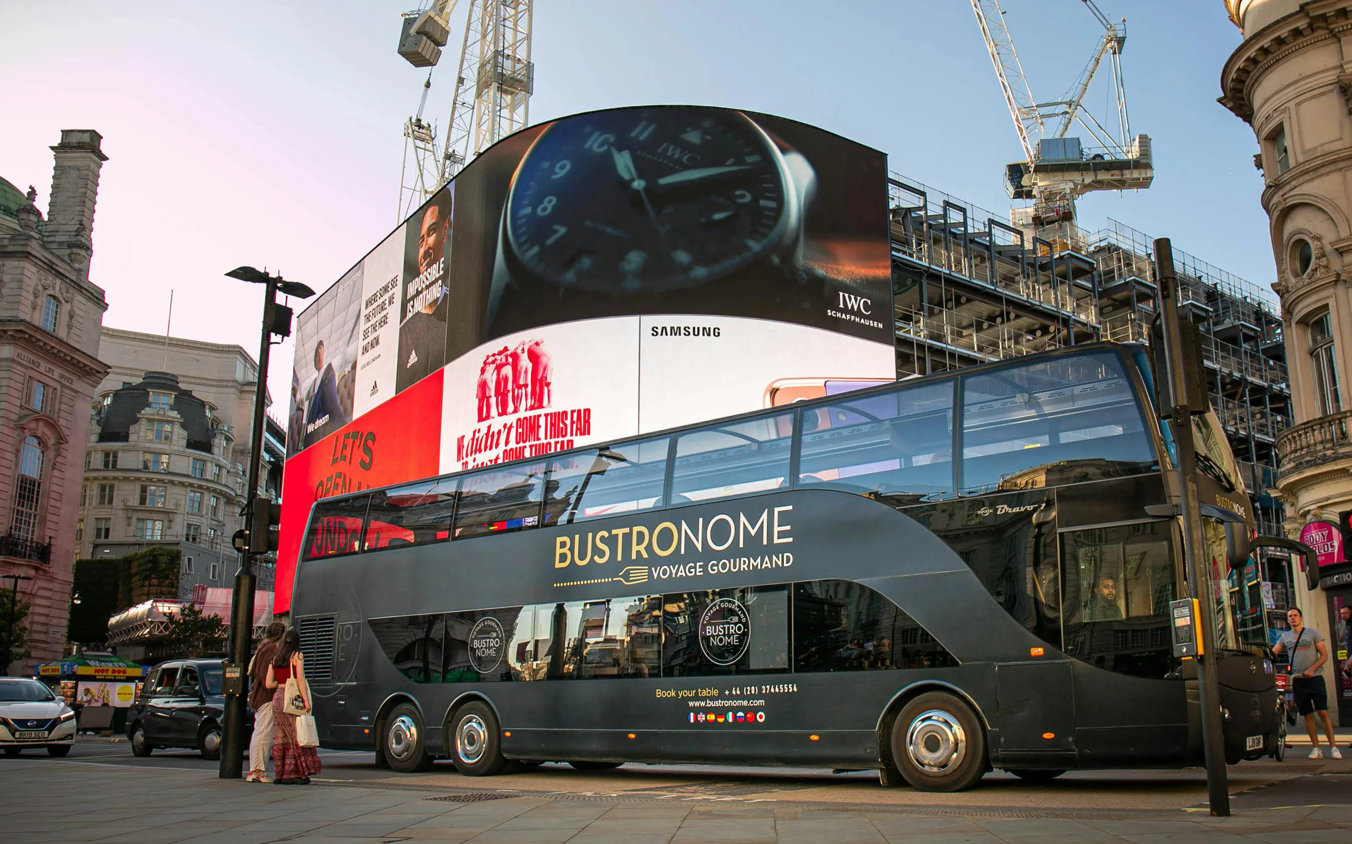 Bustronome tour bus at Piccadilly Circus, London with digital billboards in the background.