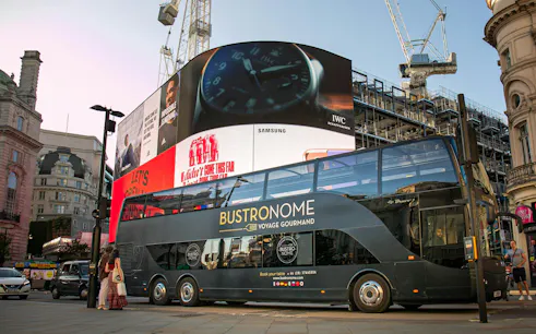 Bustronome tour bus at Piccadilly Circus, London with digital billboards in the background.