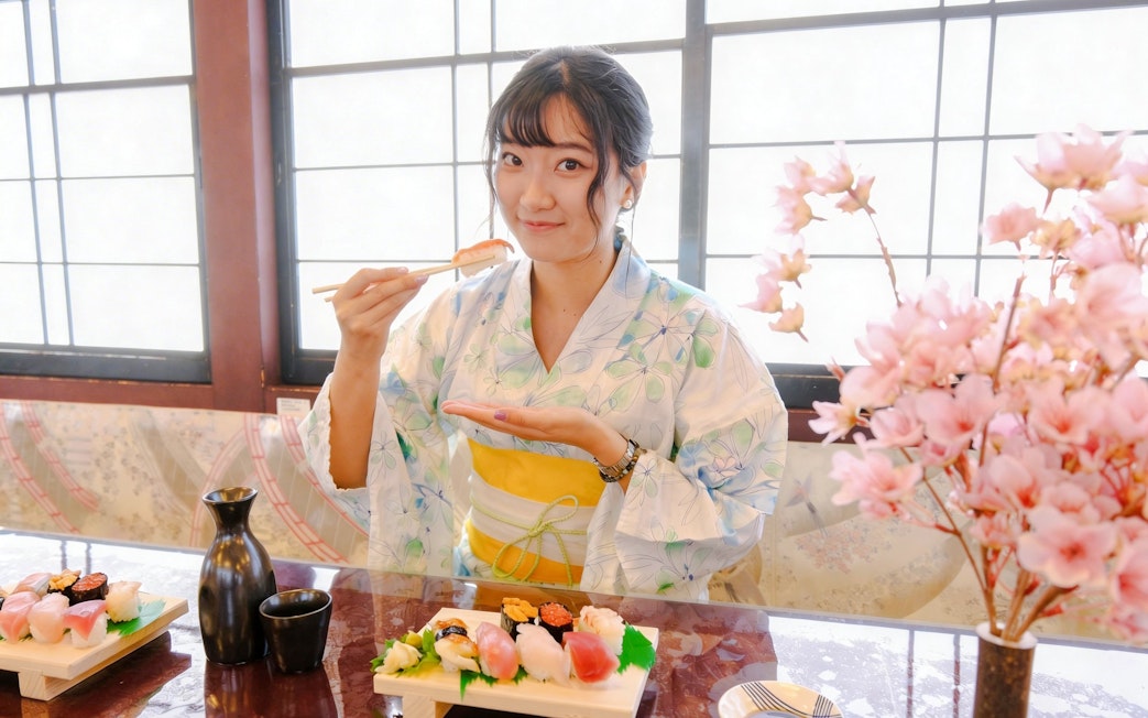 Tourist enjoying sushi on Tokyo day tour with cherry blossoms in background.