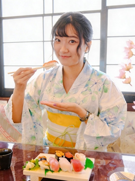 Tourist enjoying sushi on Tokyo day tour with cherry blossoms in background.