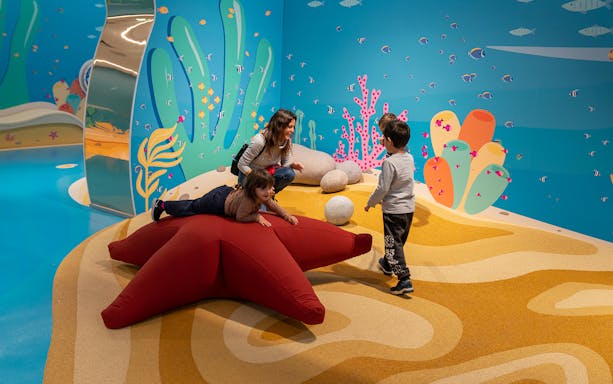Children playing on a starfish-shaped cushion in an interactive marine-themed exhibit.