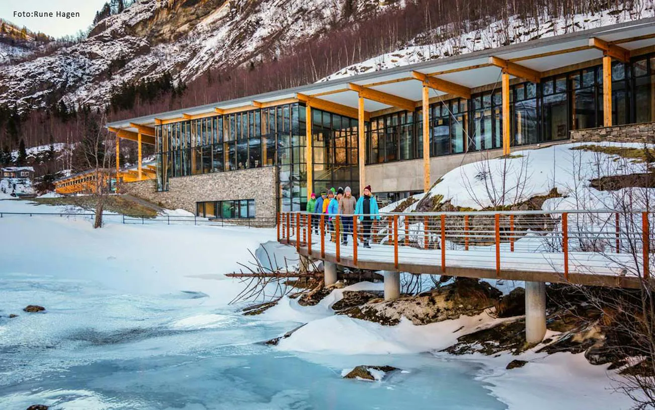 Visitors walking on a snowy path by a modern building in Geiranger during the Ålesund winter fjord cruise.
