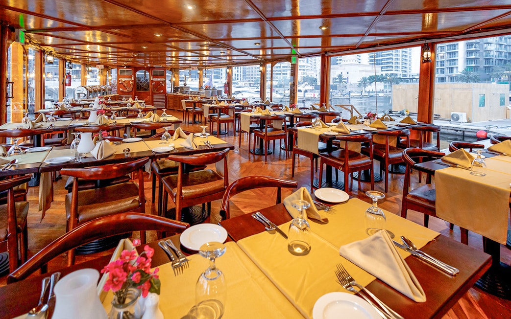 Dining setup on Alexandra Dhow Cruise in Dubai Marina with tables and city view.