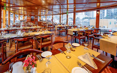 Dining setup on Alexandra Dhow Cruise in Dubai Marina with tables and city view.