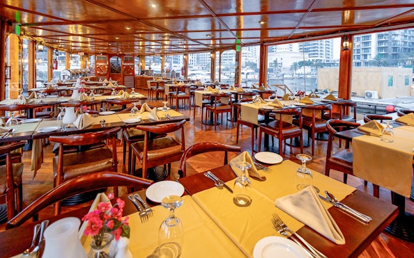 Dining setup on Alexandra Dhow Cruise in Dubai Marina with tables and city view.